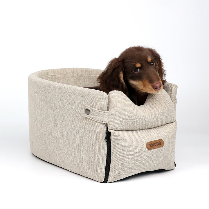 Kleine hond in een beige autostoeltje op de armleuning